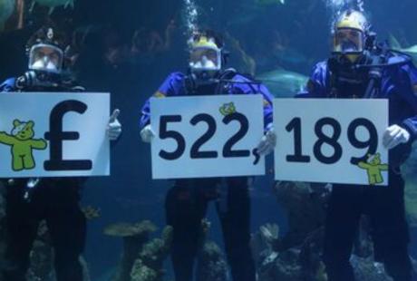 Divers in tank holding sign with amount of money raised